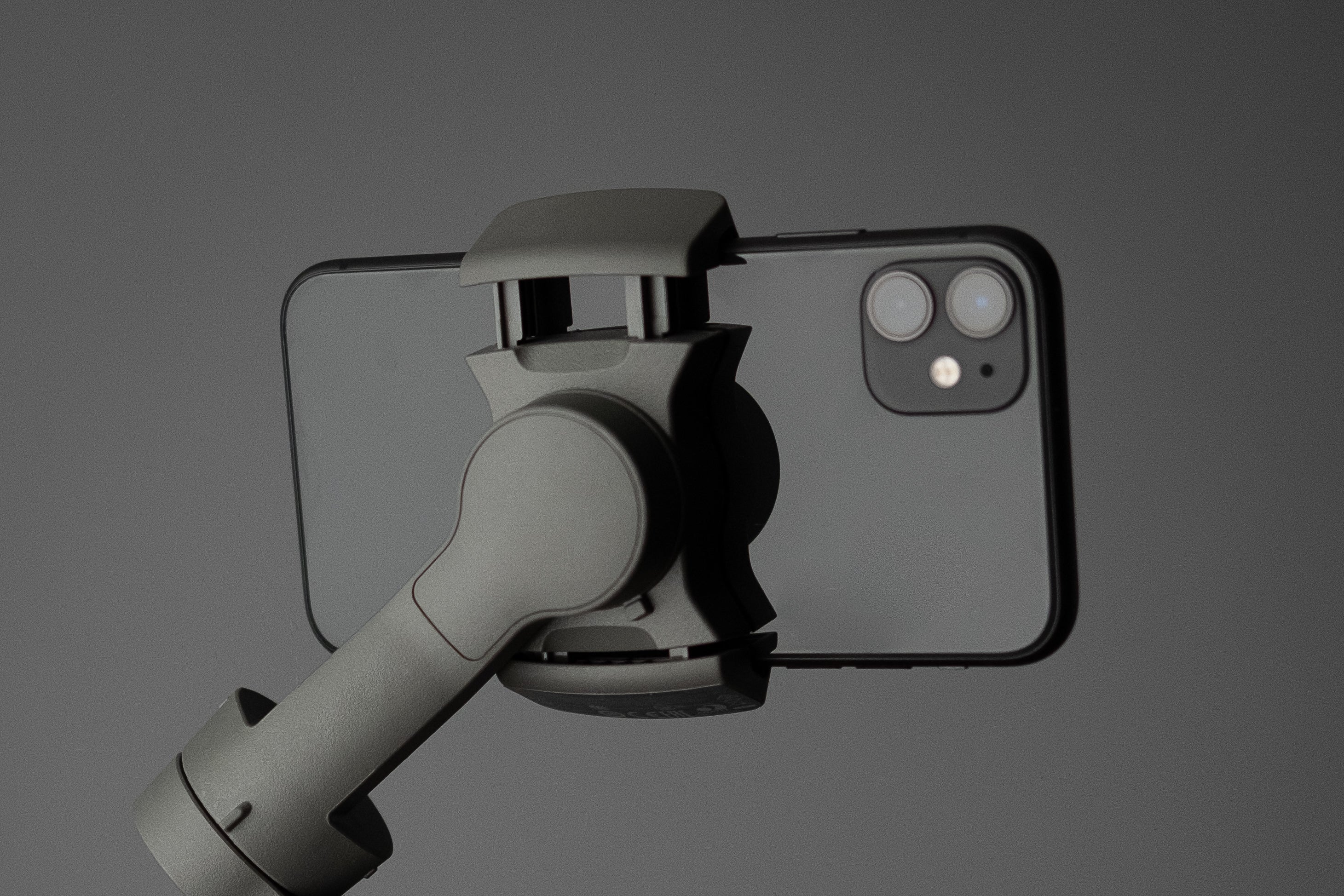 Hand holding a smartphone gimbal with a gray background